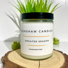 Load image into Gallery viewer, Crenshaw Candles Sweater Season candle on a wooden surface with a plant in the background

